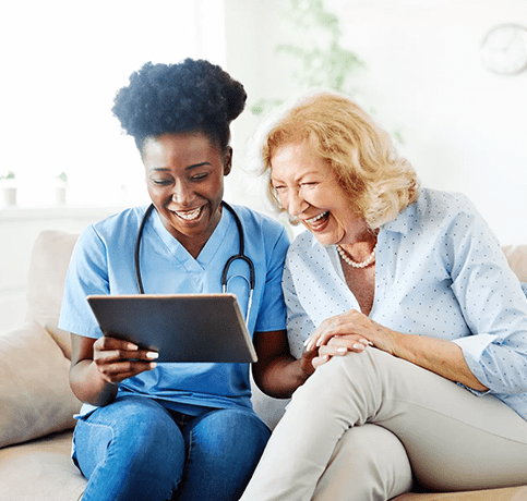 A nurse and an older woman are looking at something on the tablet.