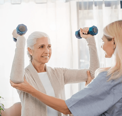 A woman is helping an older person with some exercise equipment.