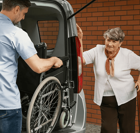 A man helping an elderly woman load her wheelchair into the back of a van.