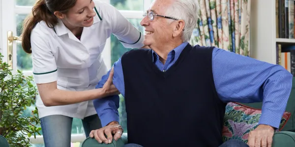 A woman is helping an older man sit in his chair.