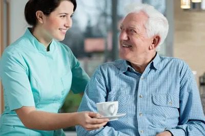 A nurse is holding a cup of coffee for an old man.