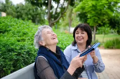 Two women sitting on a bench and one is holding an ipad