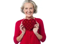 A woman holding a heart shaped pillow in front of her face.