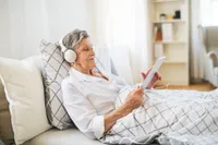 An older woman is listening to music while reading.