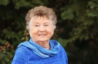 A woman in blue shirt and scarf standing next to trees.