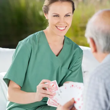 A nurse is holding cards and talking to an older man.