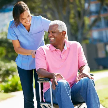 A woman is helping an older man sit in a chair.