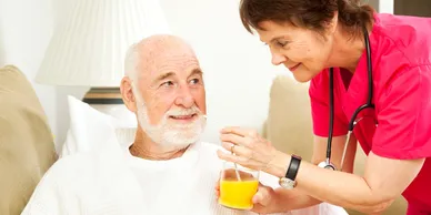 A woman is feeding an old man some orange juice.