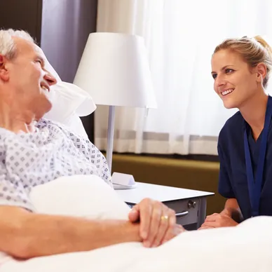 A nurse talking to an older man in hospital bed.