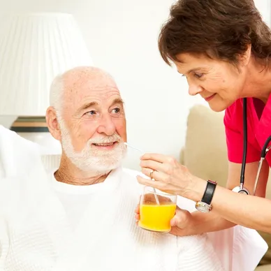 A nurse is giving an elderly man some juice.