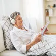 A woman in white shirt and headphones laying on bed.