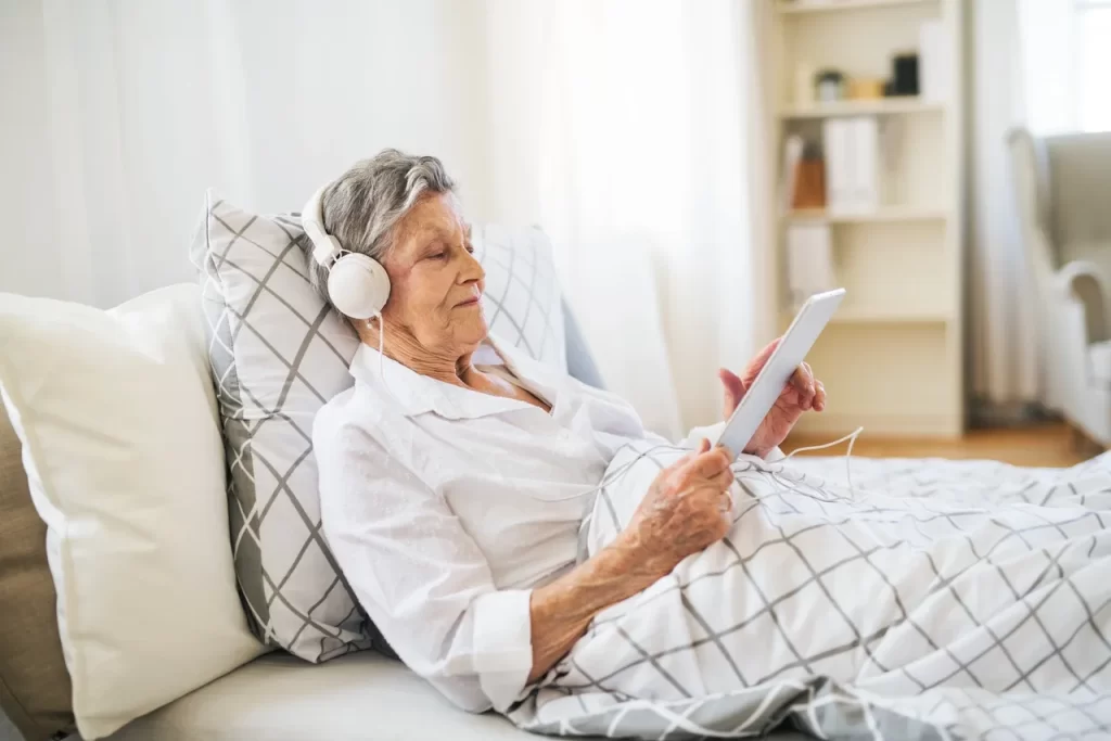 An older woman is listening to music on her tablet.