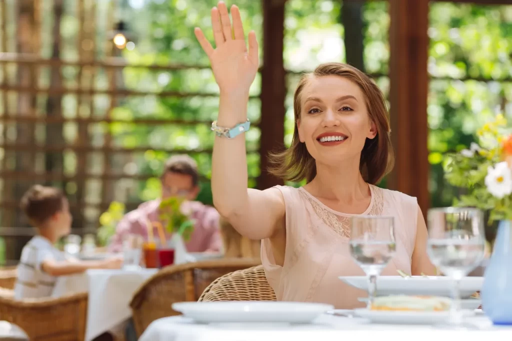 A woman sitting at an outdoor table waving.