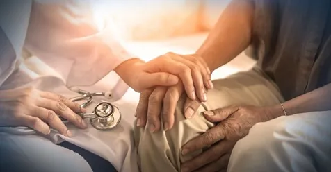 A doctor and nurse holding hands over an older patient.