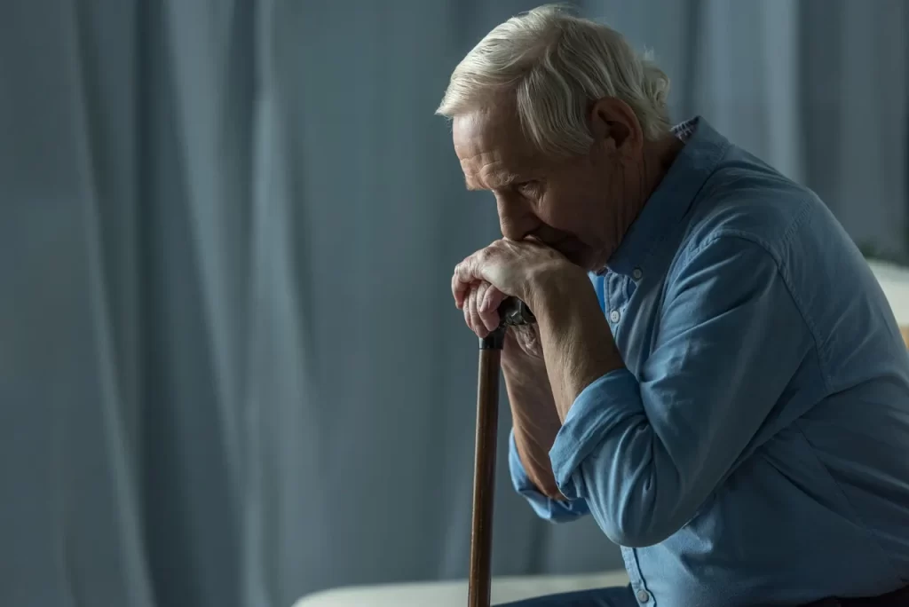 A man with his hands on the handle of a cane.