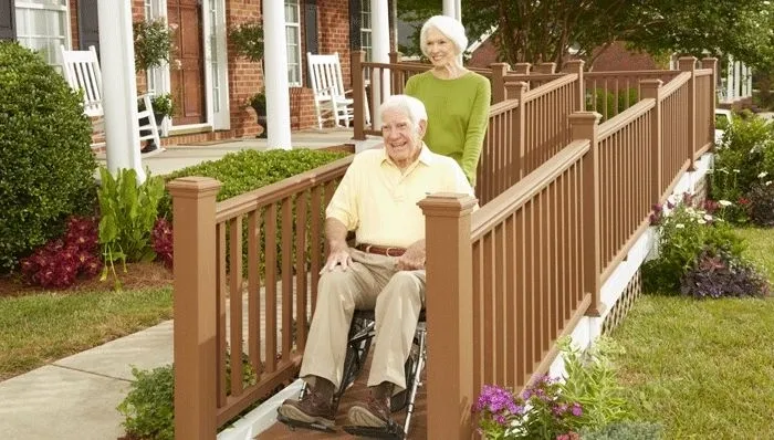 A man in a wheelchair and woman on the porch of a house.