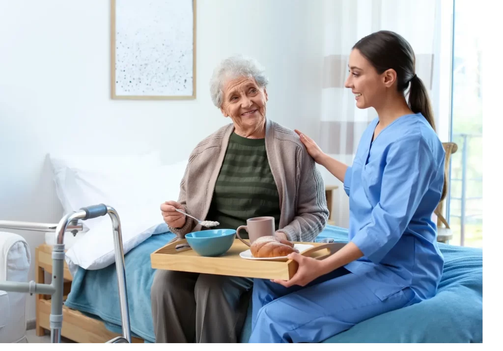 A woman in blue scrubs holding a tray with food.